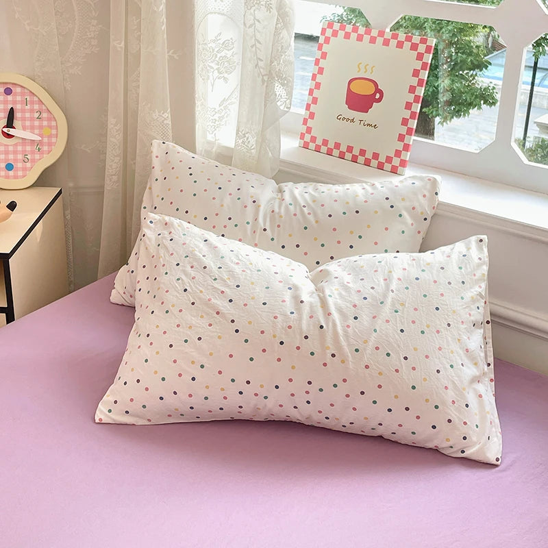 A set of white microfiber duvet cover and pillowcases with multi-colored polka dots displayed on a purple bed.