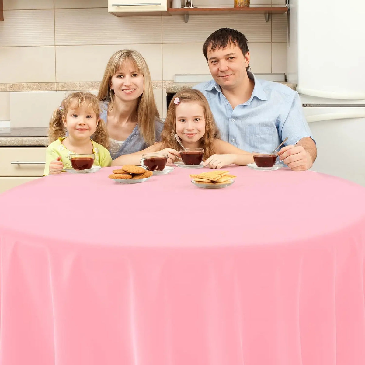 A family of four is seated around a pink table covered with a plastic disposable tablecloth.
