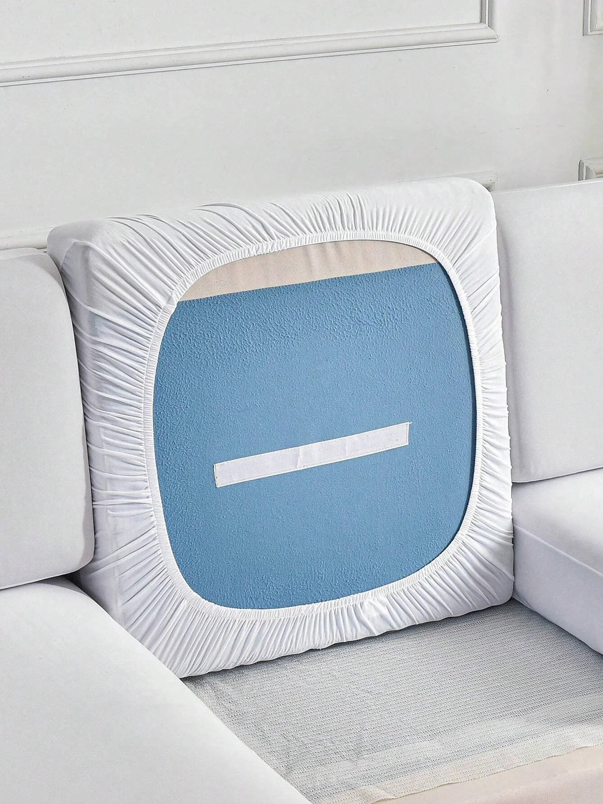 A white elastic sofa slipcover with a light blue cushion featuring a white horizontal line.
