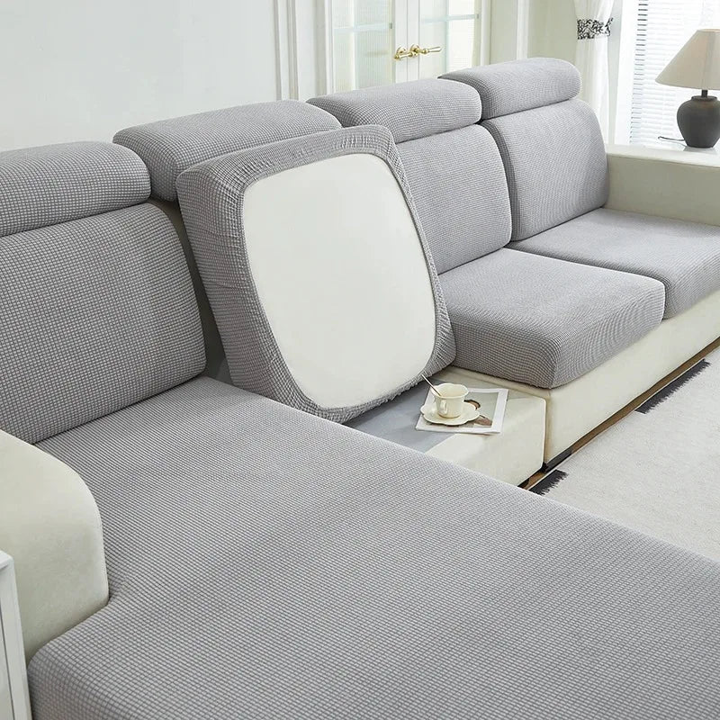 A light gray jacquard elastic sofa cushion slipcover with a white accent cushion shown in a living room setting.