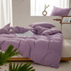 A purple minimalist duvet cover is spread on a bed with white linens and natural light.
