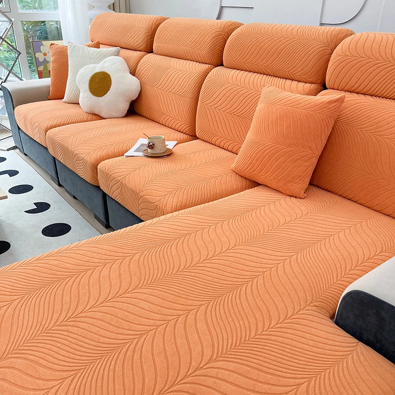 An orange jacquard stretch sofa cover featuring a wavy pattern and light cream accent pillows.