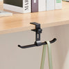 A black adjustable aluminum alloy desk hook with dual clips is hanging on a light wood shelf.