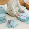 A person is organizing travel storage with a light blue fabric organizer set on a bed.