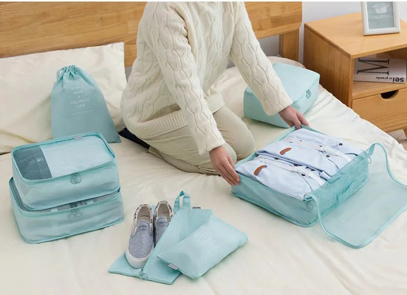 A person is organizing travel storage with a light blue fabric organizer set on a bed.