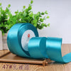 A roll of teal satin ribbon for gift wrapping and DIY crafts, resting on a wooden surface with green foliage in the backgroun