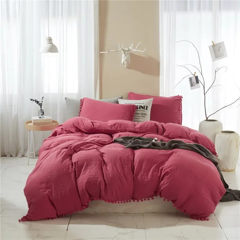 A pink soft washed duvet cover set with pom-pom decoration displayed on a bed in a bright room.