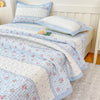 A floral quilted bedspread featuring white and light blue stripes and pink flowers on a bed.