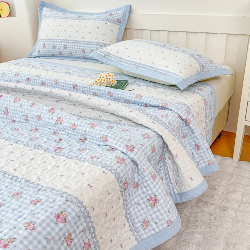 A floral quilted bedspread featuring white and light blue stripes and pink flowers on a bed.