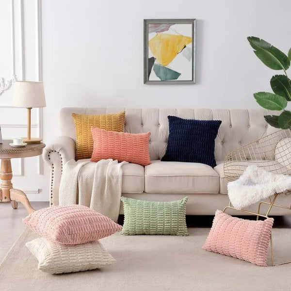 A set of two pink and yellow velvet throw pillow covers displayed on a light beige sofa.