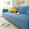 A light blue stretchable sofa cover with a vertical line pattern featuring a yellow stuffed animal and a white mug.