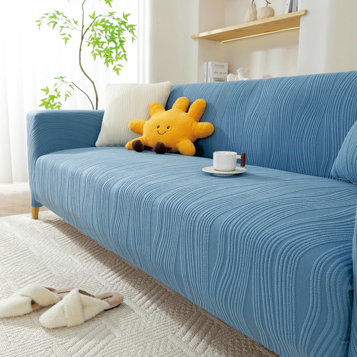 A light blue stretchable sofa cover with a vertical line pattern featuring a yellow stuffed animal and a white mug.