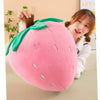 A pink plush strawberry throw pillow with green leaves is being held by a person.