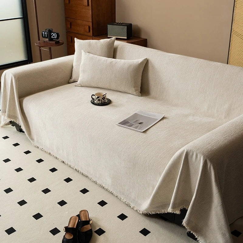A cream-colored minimalist chenille sofa cover draped over a light beige sofa with decorative pillows and a magazine.