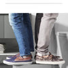 A pair of brown and gray leather dress shoes are placed on a modern stool in front of a toilet.