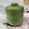 A spool of shimmering green glitter metallic yarn for crochet and knitting resting on pink flowers.