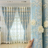 Light blue floral sheer curtains with lace trim hanging in a window frame