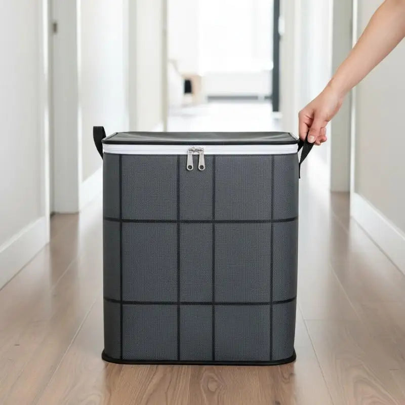 A hand is lifting a gray fabric storage bag with black handles in a hallway.