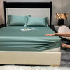 A luxury bed featuring a teal fitted sheet, pillows, and a light beige mattress, set against a dark headboard.