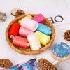 A wooden bowl filled with ten rolls of colorful polyester sewing thread in various shades of pink, yellow, red, and blue.