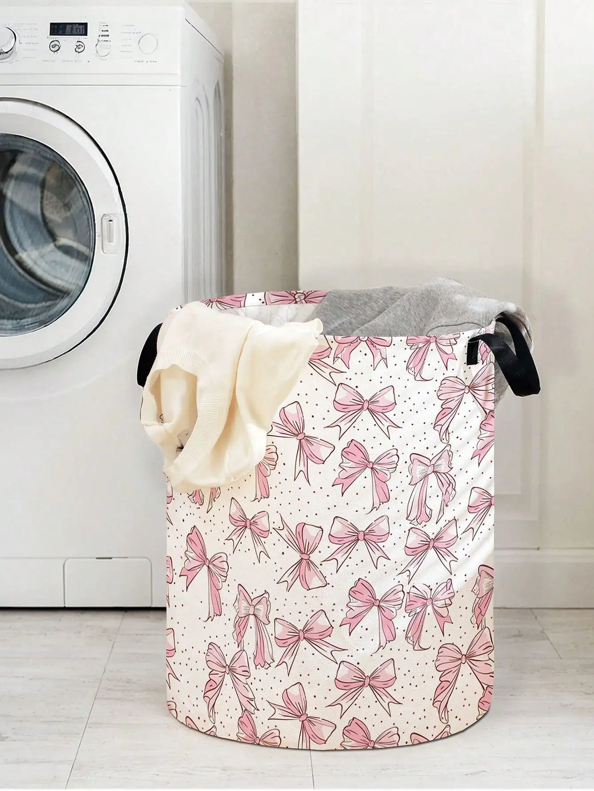 A pink and white foldable canvas laundry basket decorated with a pattern of pink bows, placed next to a washing machine.