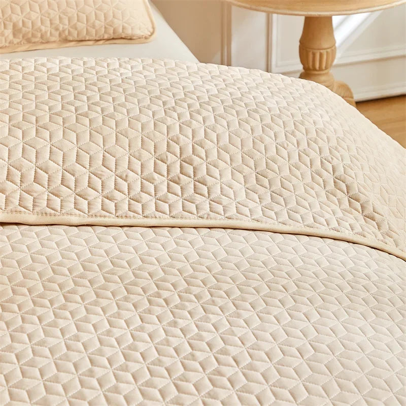A close-up of a beige quilted bedspread featuring a diamond pattern on a queen bed.