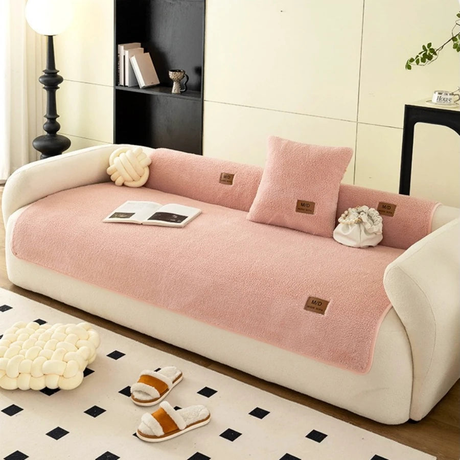 A pink sherpa anti-slip sofa cover displayed on a white sofa with decorative pillows and slippers.