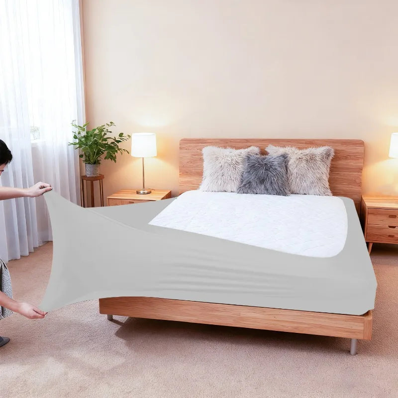 A light gray high-stretch elastic box spring cover is displayed on a wooden bed frame with fluffy pillows.
