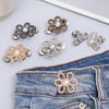 A collection of adjustable metal waist clips in gold and silver tones displayed on a denim jean fabric.