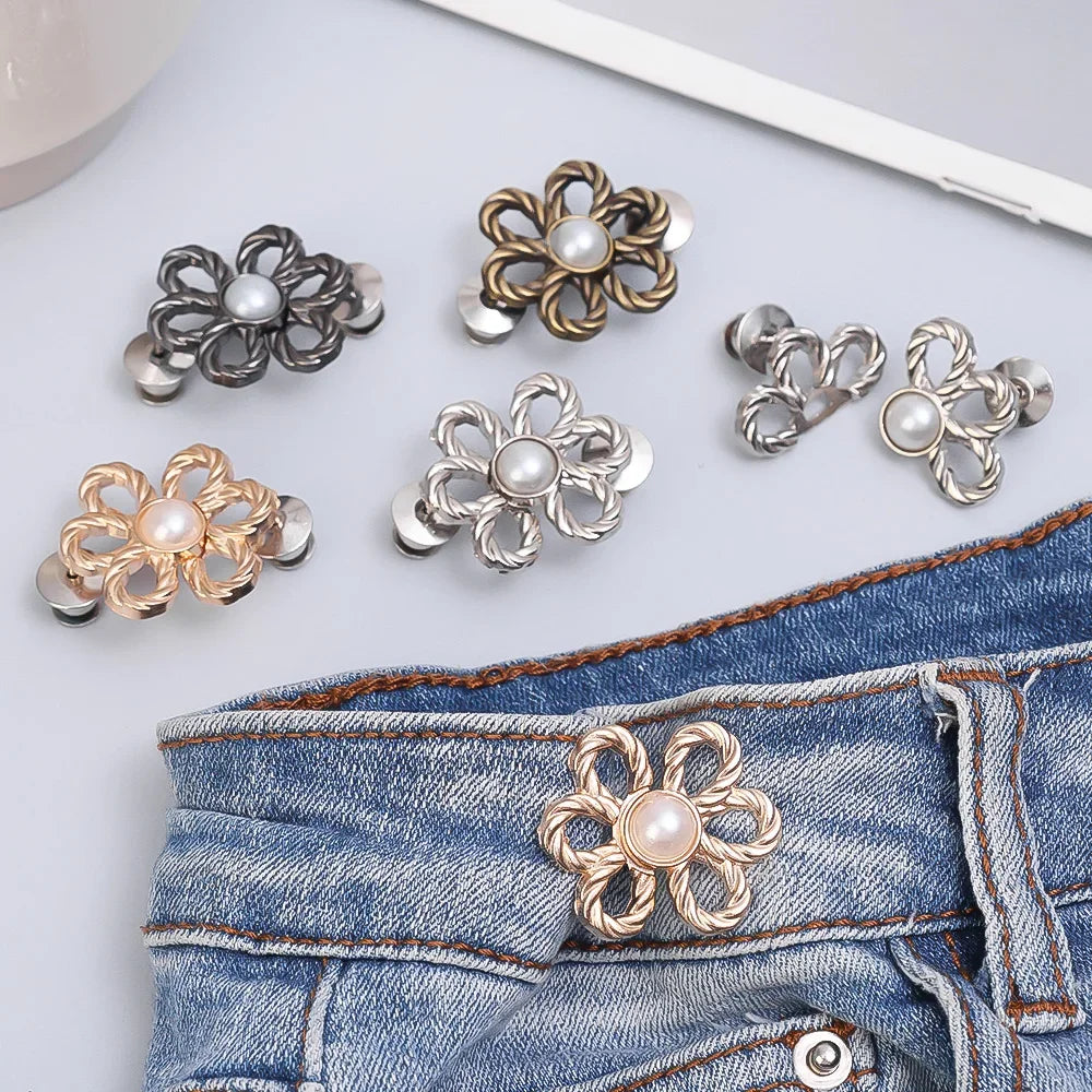 A collection of adjustable metal waist clips in gold and silver tones displayed on a denim jean fabric.