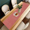 A light wood dining table set with a red and white checkered table runner, chairs, and a vase of greenery.