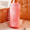 A rolled pink cotton muslin swaddle blanket with white sunburst patterns resting in a woven basket.