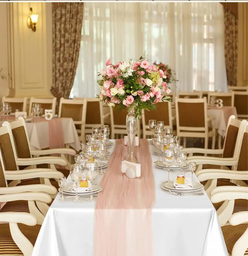 A white rectangular table set with a pink satin runner and glassware in an elegant dining room setting.