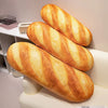 Three golden brown soft plush French baguette pillows displayed on a white shelf.