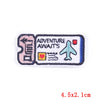 Pink embroidered iron-on patch featuring an adventure theme with text and a airplane icon