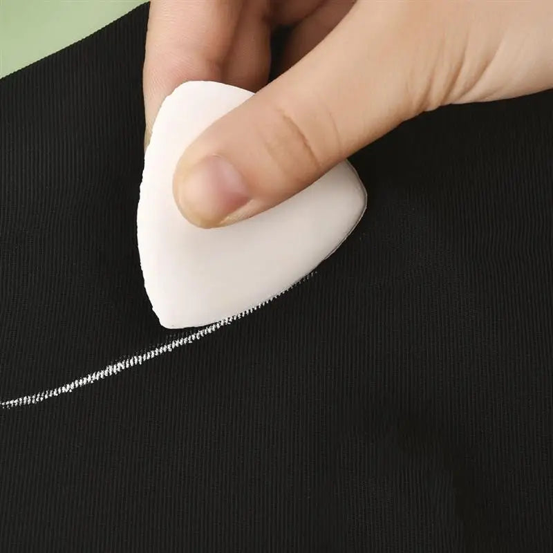 A hand is holding a white erasable fabric chalk marker on a black fabric.