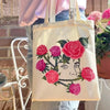A beige canvas tote bag featuring a detailed floral design of pink and red roses.
