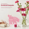 A pink floral arrangement with a personalized plaque keepsake and a small glass on a white surface.
