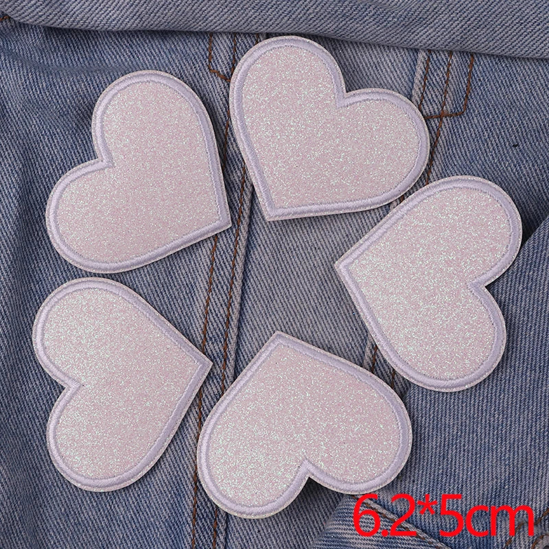 Five pink glitter iron-on embroidered love heart star patches laid on a denim fabric background