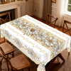 A white floral tablecloth with gold accents is displayed on a wooden table in a well-lit room.