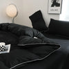A black duvet cover set with a white trim is displayed on a bed, next to a lamp and framed art.