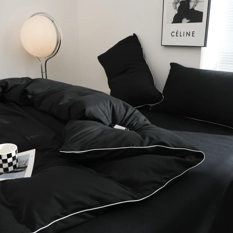 A black duvet cover set with a white trim is displayed on a bed, next to a lamp and framed art.