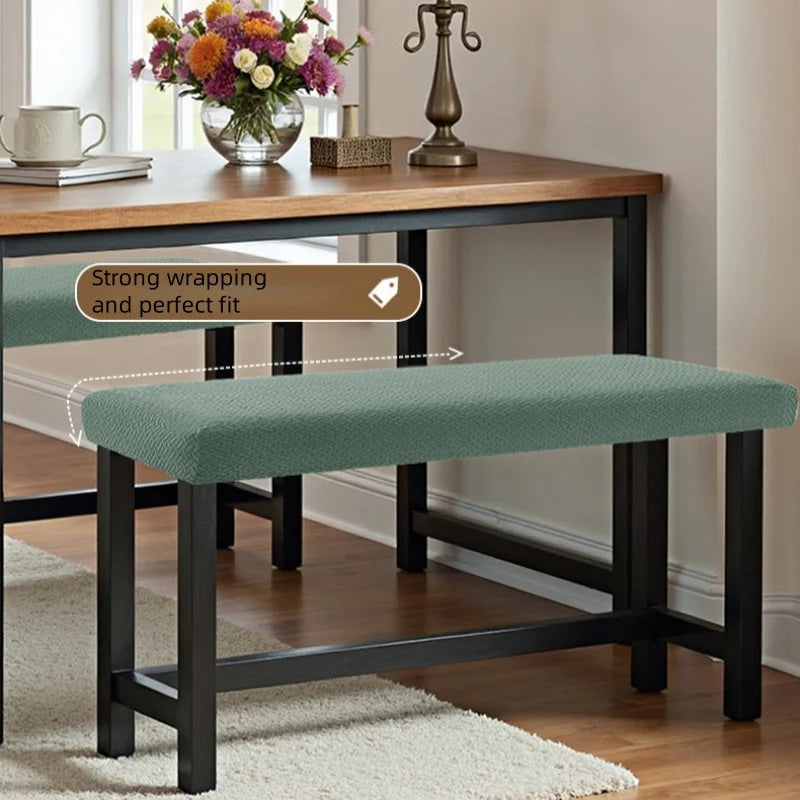 A dark wood dining table with a green upholstered bench cover and a decorative floral arrangement.