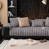 A gray, tufted sofa seat cushion rests on a light-colored rug with a white faux fur throw and small decorative balls.