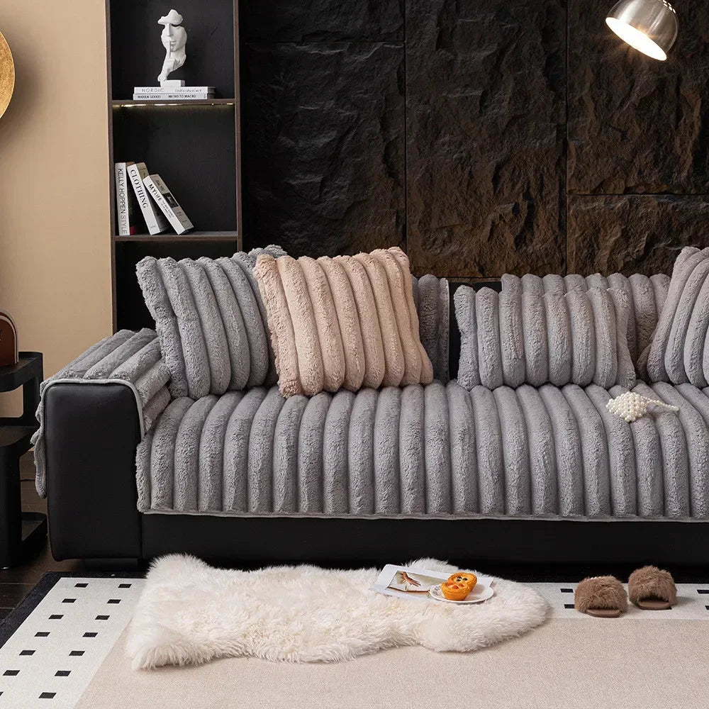 A gray, tufted sofa seat cushion rests on a light-colored rug with a white faux fur throw and small decorative balls.