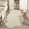 A cream colored irregular plush area rug placed on a light wood floor in a bright room.