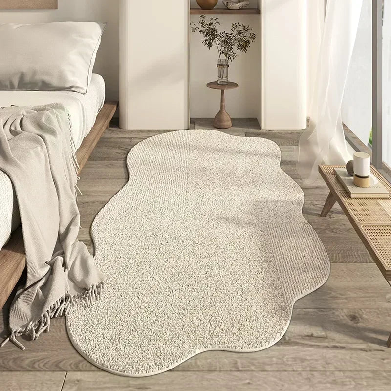A cream colored irregular plush area rug placed on a light wood floor in a bright room.