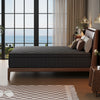 A dark gray hybrid memory foam and pocket spring mattress resting on a wooden bed frame in a modern bedroom with large window