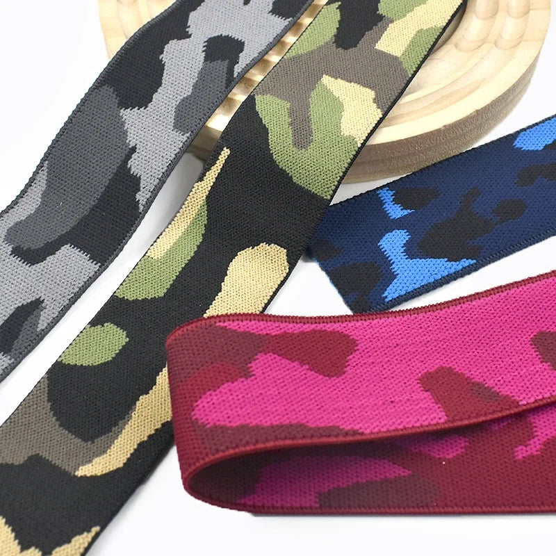 A variety of camouflage patterned elastic stretch ribbons in black, olive green, and pink are displayed.