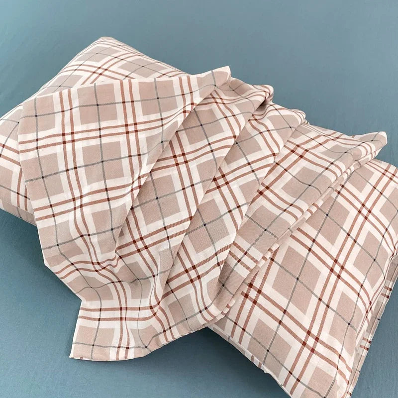 A set of two plaid beige and brown pillow covers folded on a blue surface.